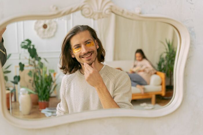 A man with long hair and under-eye patches smiling at his reflection in a mirror. Women shut down creepy men.
