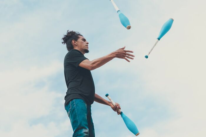A man juggling blue clubs against a light sky, showing an impressive skill. Many women shut down creepy men.
