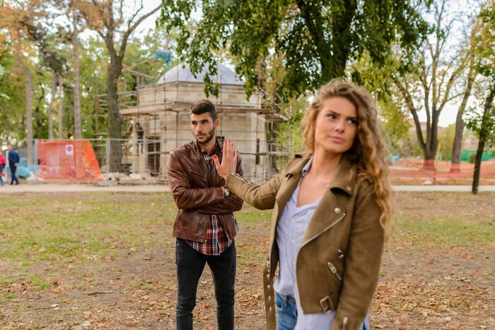 A woman extending her hand to stop a man in a park. Women shut down creepy men with savage ways.