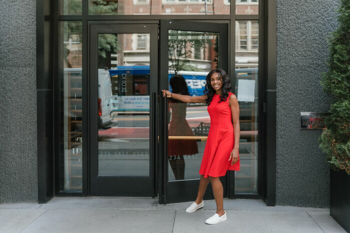 A smiling woman in a red dress opening a door, representing the empowerment of women who shut down creepy men.