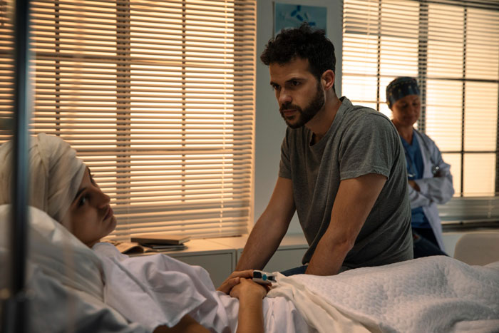 A fiancé visits a woman in the ICU after her medical emergency, with a nurse in the background. A fiancé visits a woman in the ICU after her medical emergency, with a nurse in the background.