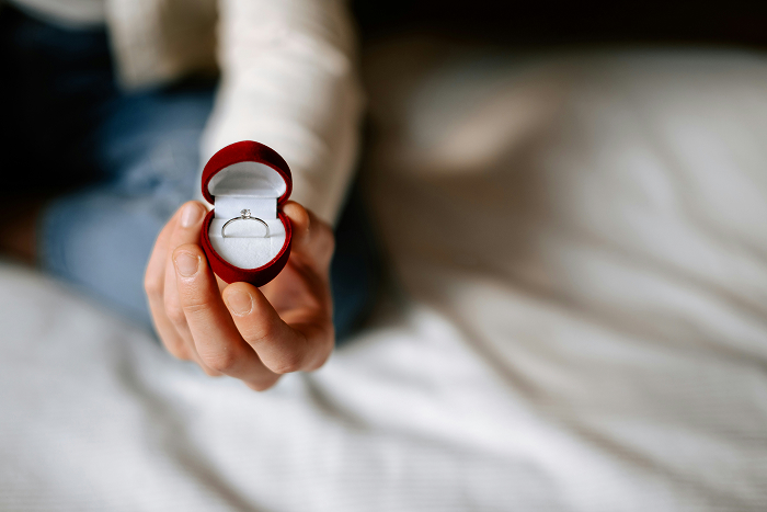 A hand holds an open ring box with a diamond ring, symbolizing a marriage proposal and open relationship. A hand holds an open ring box with a diamond ring, symbolizing a marriage proposal and open relationship.