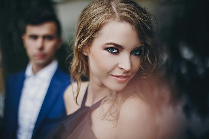 A man in a suit looks on as a woman in a black dress smiles, suggesting an open relationship challenge. A man in a suit looks on as a woman in a black dress smiles, suggesting an open relationship challenge.