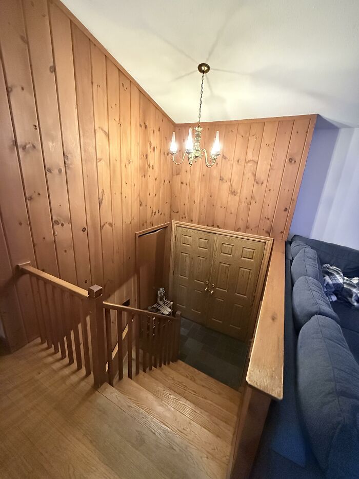 A view from the top of the stairs looking down towards a wooden double door, showcasing home design choices.