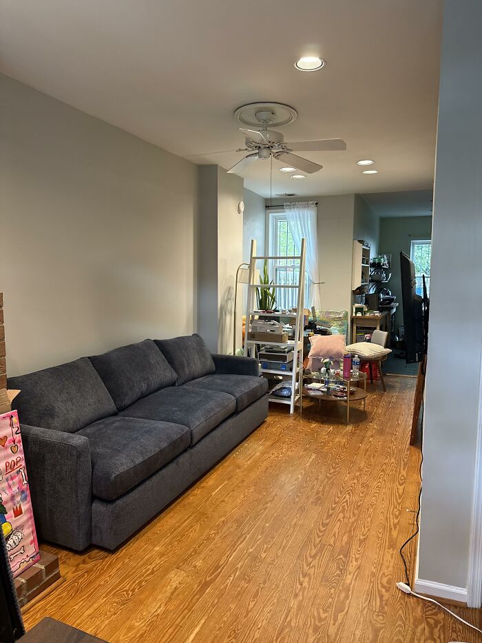 A narrow living room home design with a gray sofa, hardwood floors, and a ceiling fan.