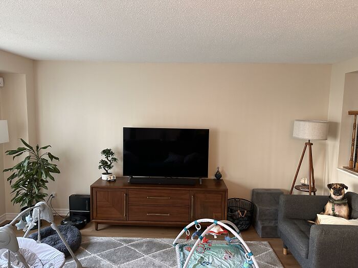A modern living room showcasing home design choices with a large TV, entertainment unit, and baby playmat, inviting honest opinions.