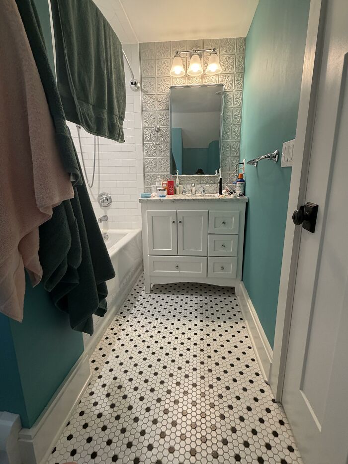 A bathroom with unique home design choices, including teal walls, a white vanity, and black and white hexagon floor tiles, for honest opinions.