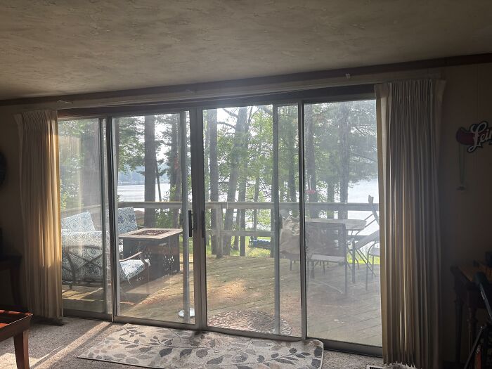 A living room with sliding glass doors opening to a deck overlooking a lake, displaying home design choices for honest opinions.