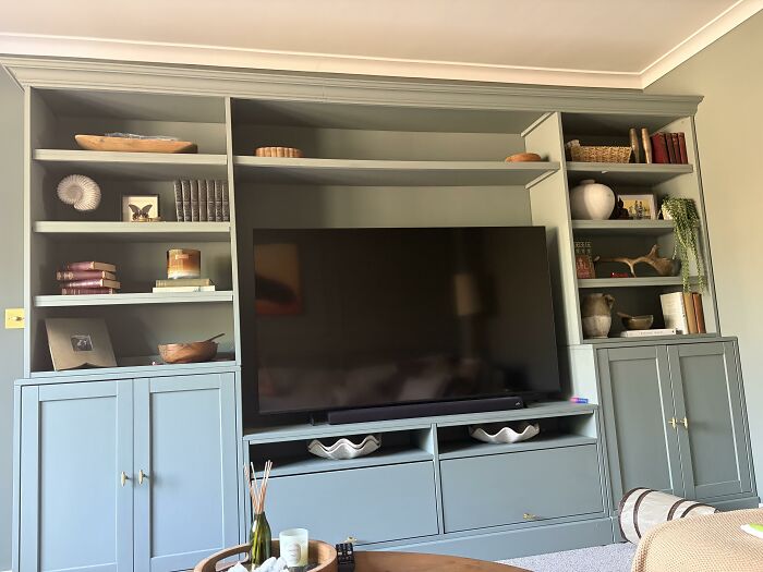 A built-in entertainment unit in a soft green color, filled with books and decorative items, highlighting home design choices.