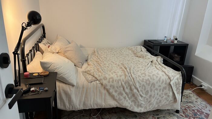 A bedroom with a black metal bed frame, white bedding, and a leopard print throw blanket, reflecting home design choices.