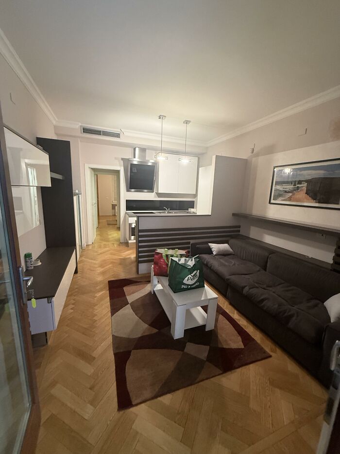 A modern living area with a brown sectional sofa, a white coffee table, and a kitchen visible in the background, showing home design choices.