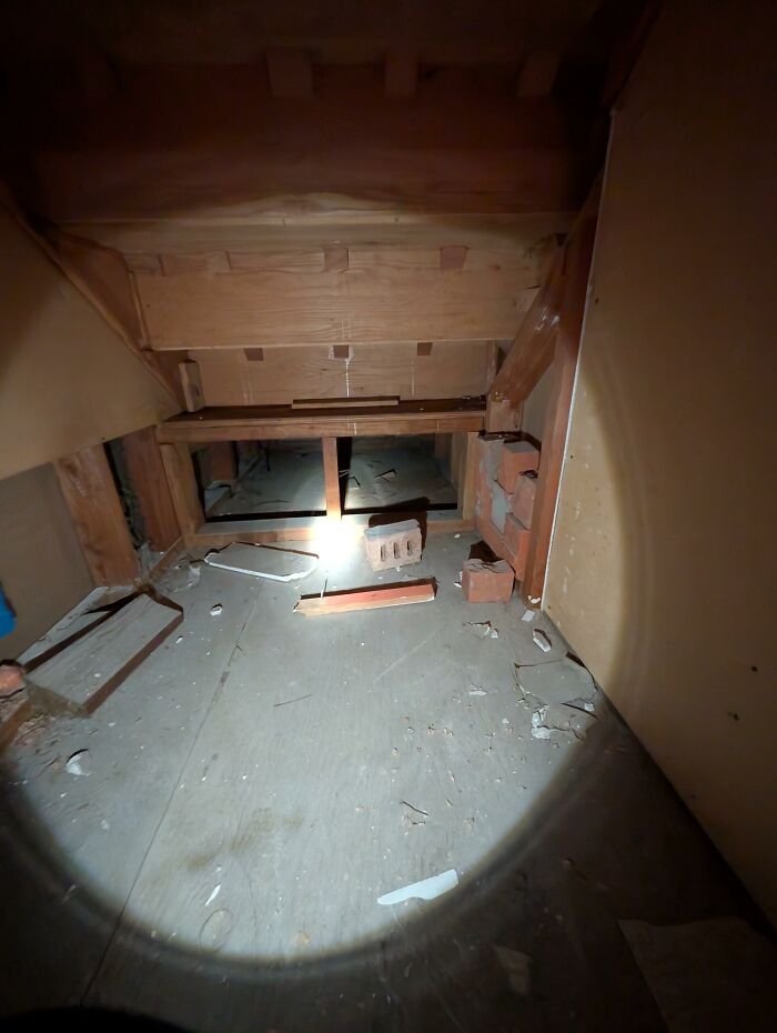 A dimly lit crawl space with exposed wood beams and scattered debris, part of honest home design choices.