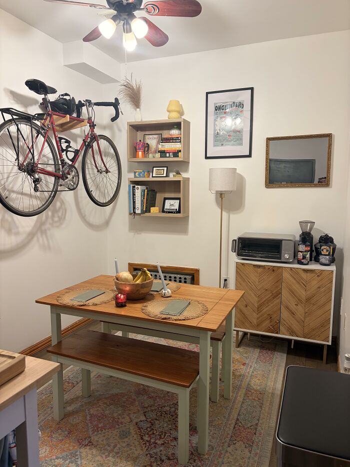 A cozy dining area with a hanging bicycle, shelves, and a patterned rug, highlighting home design choices.