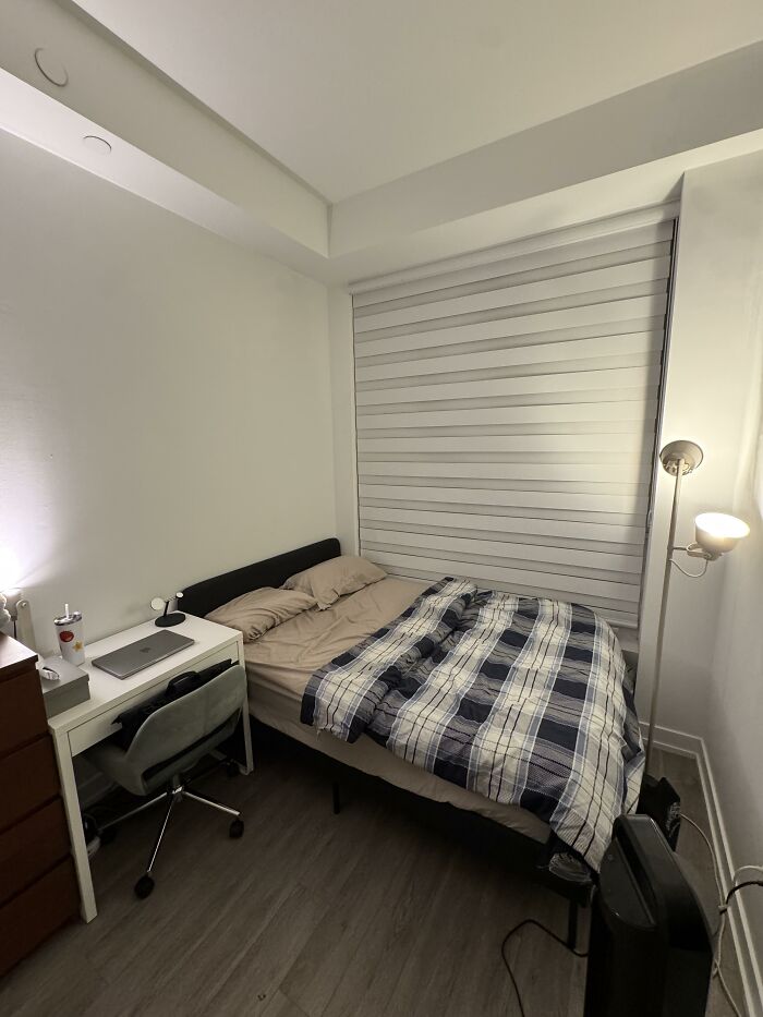 A compact bedroom with a bed, desk, and floor lamp, demonstrating personal home design choices.