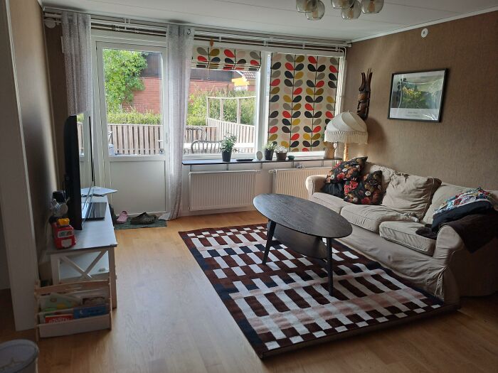 A living room with a beige couch, patterned rug, and windows featuring colorful curtains, showcasing home design choices.