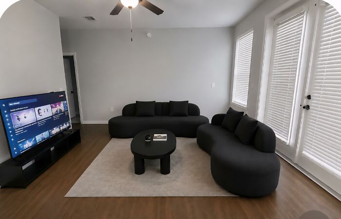 A modern living room showing home design choices with a large TV, black sofas, and a white rug.