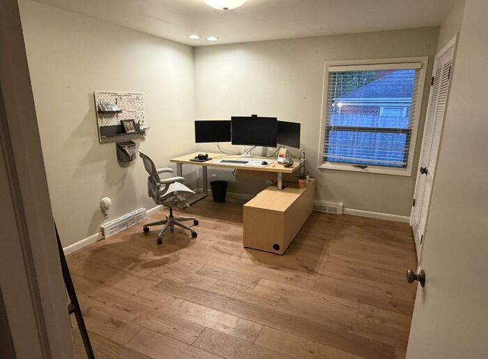 Home office featuring a light wood desk with multiple monitors, an office chair, and wooden floors, part of home design.
