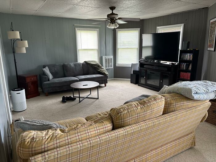 Living room with a gray couch, plaid couch, television, and ceiling fan, showcasing home design choices.