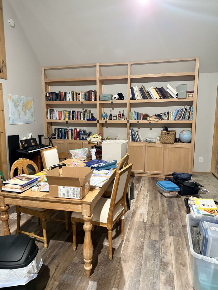 A room with a wooden table full of items and a large built-in bookshelf, reflecting personal home design choices.