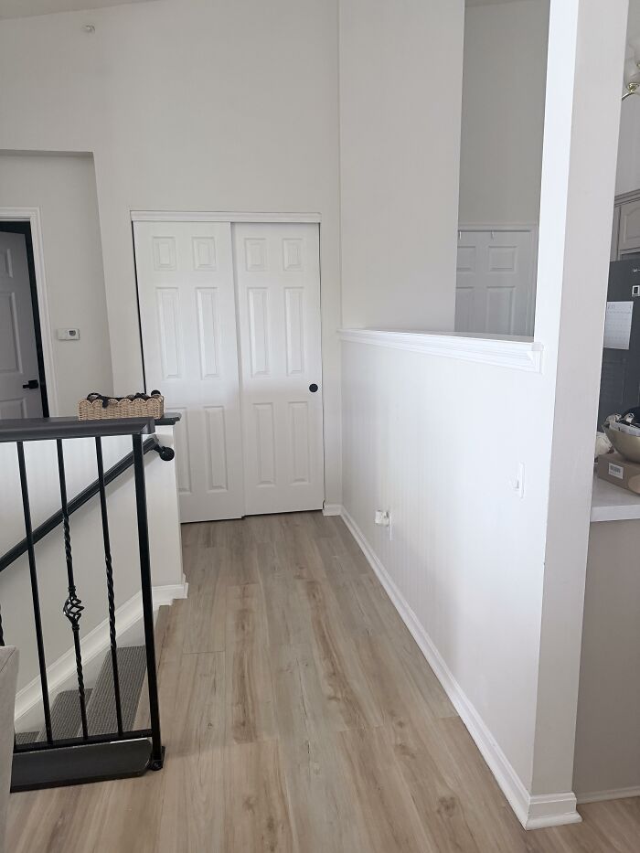A bright hallway with light wood flooring, white walls, and a black metal railing, part of a modern home design.
