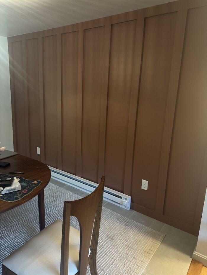 Brown accent wall with board and batten paneling in a home design, next to a round dining table and chair.