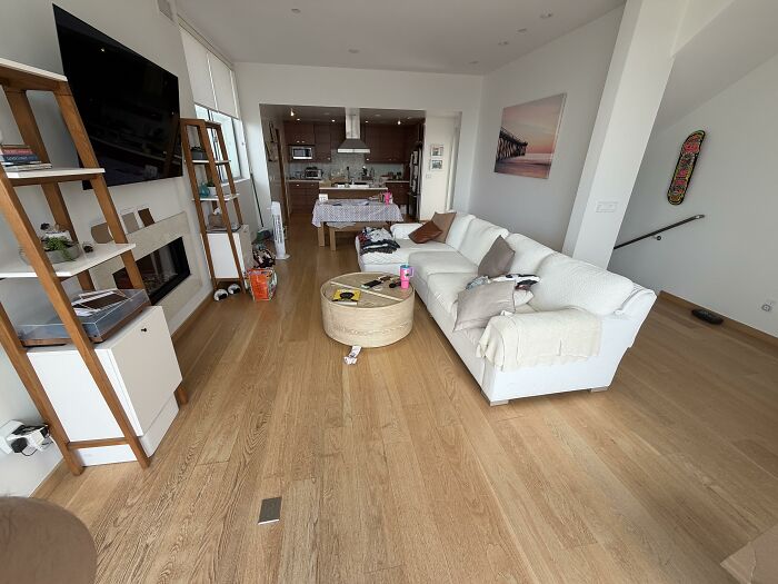 A spacious living room with an open home design plan, featuring a white couch, wooden shelves, and light hardwood floors.
