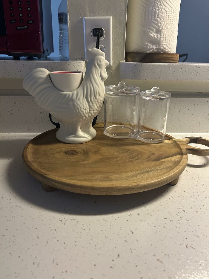 A kitchen counter displaying home design choices: a white ceramic rooster, clear containers, and a wooden tray.