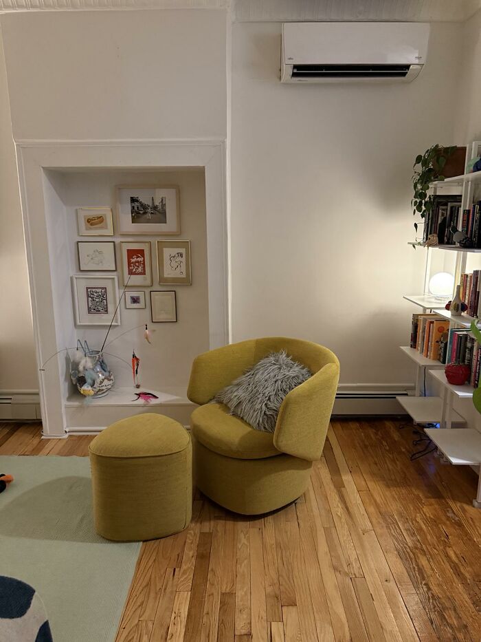 A cozy home design featuring a mustard armchair, a matching ottoman, and an alcove filled with framed art.
