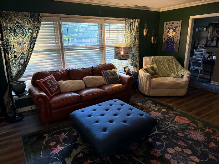 A cozy living room featuring a brown leather sofa, large blue ottoman, and patterned curtains, highlighting home design choices.
