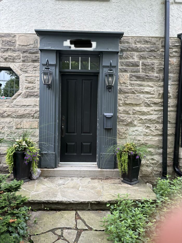 A stately dark gray front door framed by decorative columns and two large planters, exemplifying home design choices.