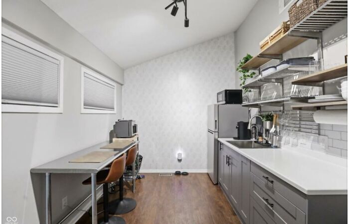 A modern kitchen displaying home design choices, with grey cabinets, open shelving, and a small breakfast bar.
