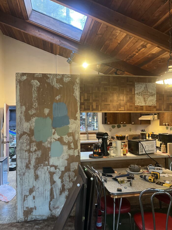 A kitchen area undergoing renovation with exposed wooden beams, a partially stripped wall, and various tools, depicting home design choices.