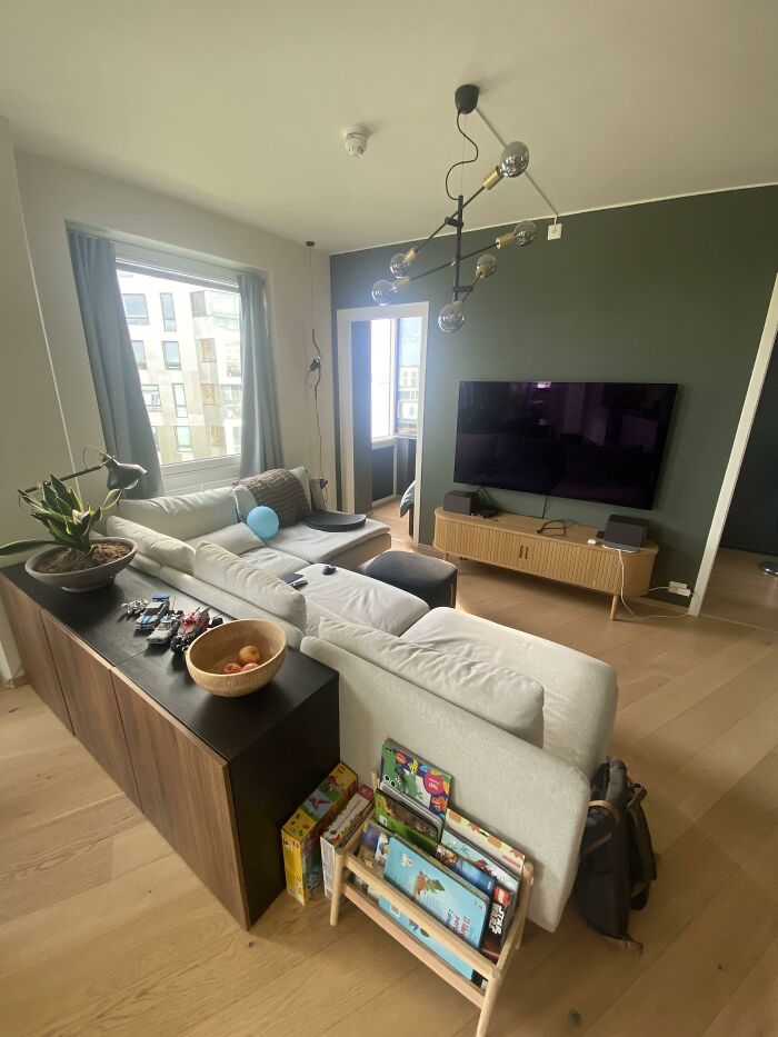 A contemporary living room featuring a large sectional, a modern light fixture, and a dark green accent wall, showcasing home design choices.