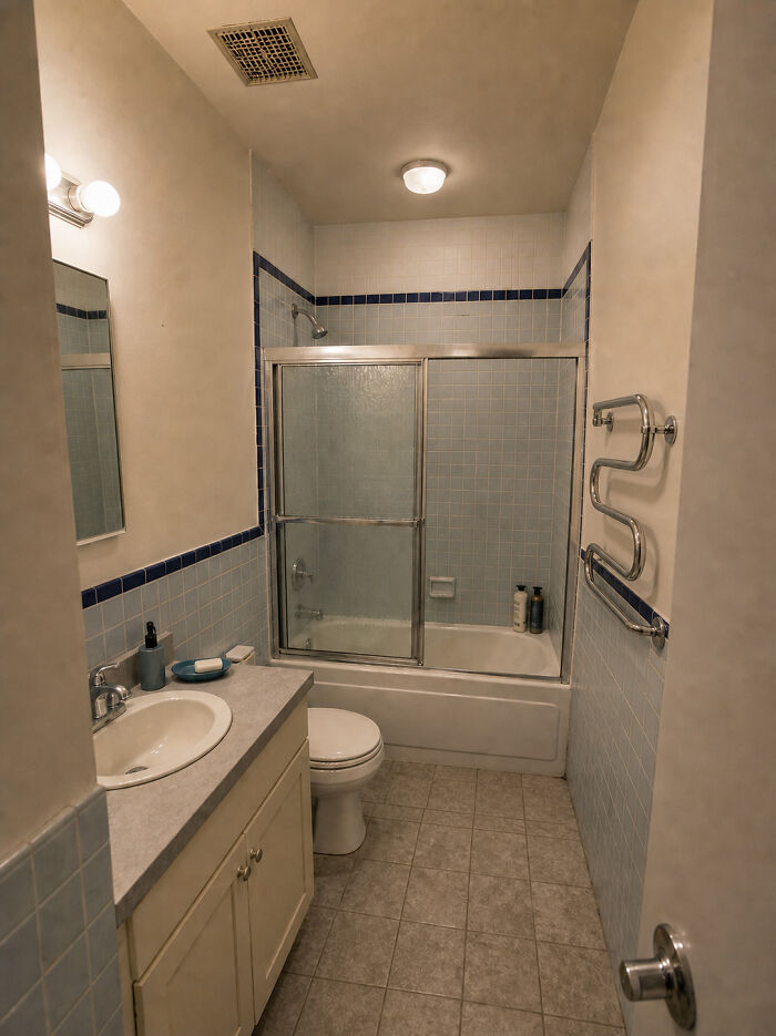 A small bathroom with blue tiled walls, a shower-tub combo, and a single vanity, showing home design choices.