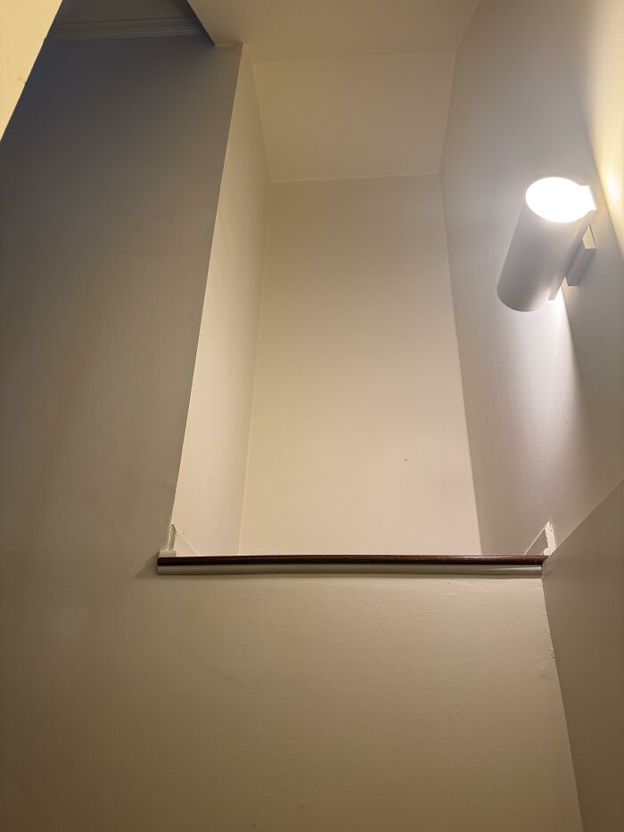 A narrow hallway or stairwell with a single wall-mounted light fixture, reflecting home design choices.