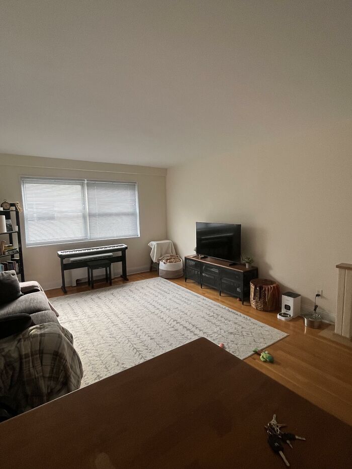 A living room with a gray couch, a piano, and a TV stand, showcasing home design choices.