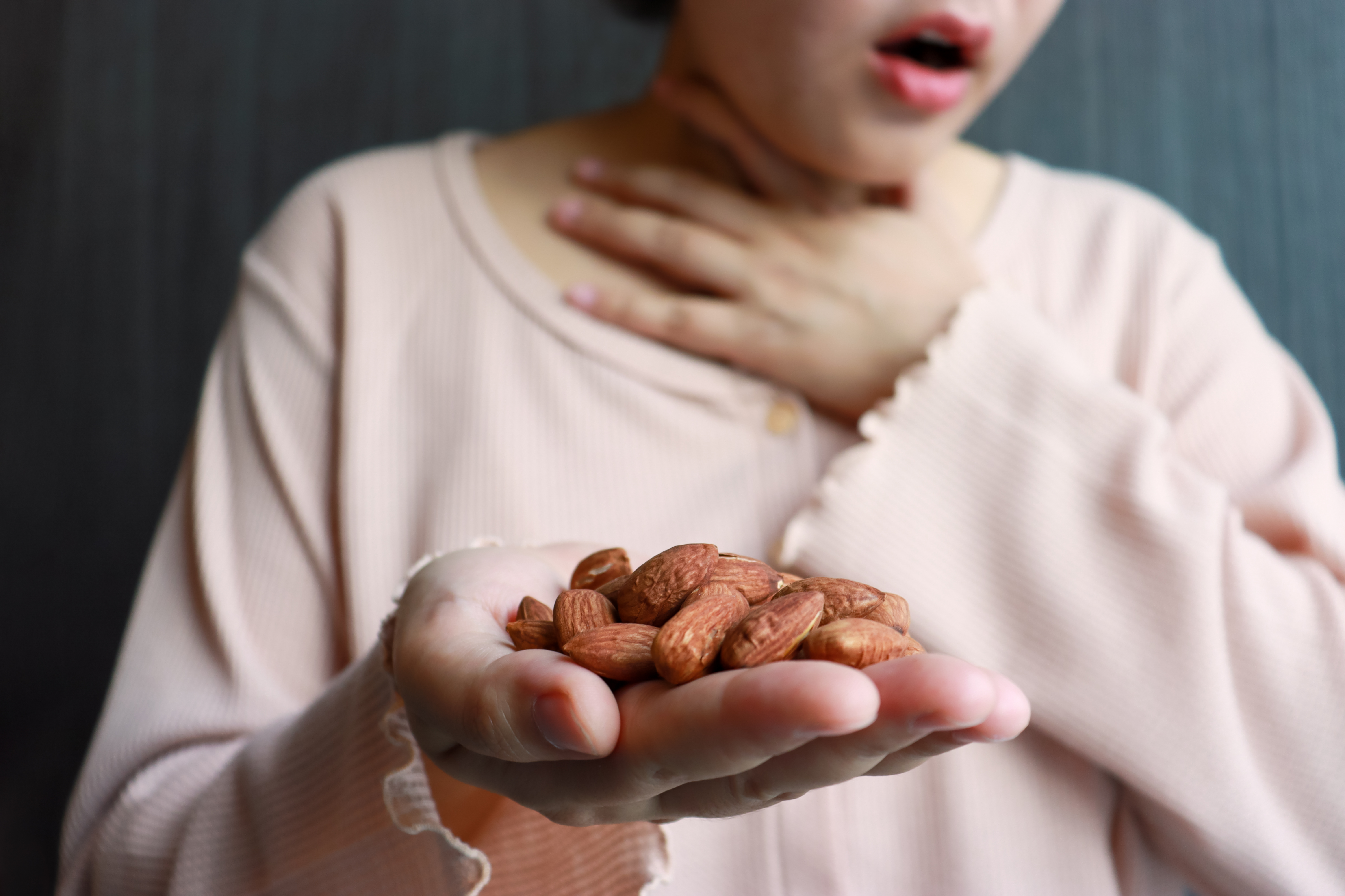 A woman holds nuts in her hand, clutching her throat with the other, concerned about her allergy. A woman holds nuts in her hand, clutching her throat with the other, concerned about her allergy.