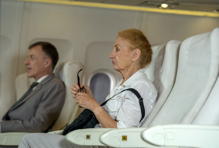 Elderly passengers on a plane, looking upset, regretting stealing seats next to a very large man. Elderly passengers on a plane, looking upset, regretting stealing seats next to a very large man.