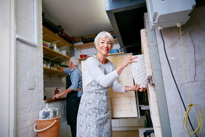 Smiling woman removing a ceramic piece from a kiln, showing family tradition and craft.