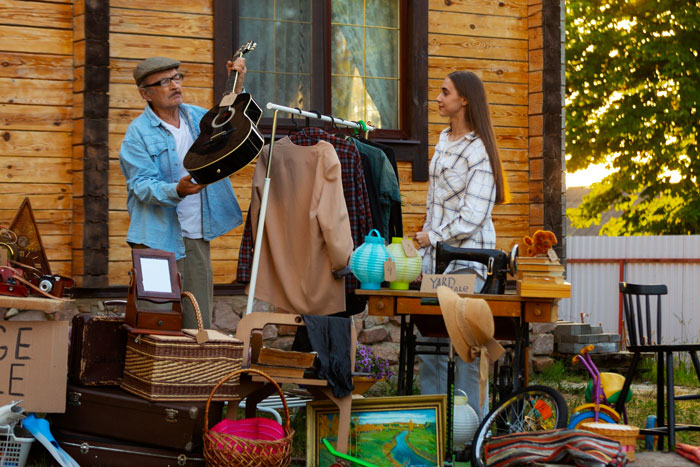 A man showing a guitar to a woman at a yard sale, symbolizing the family free table tradition shut down by the homeowner.