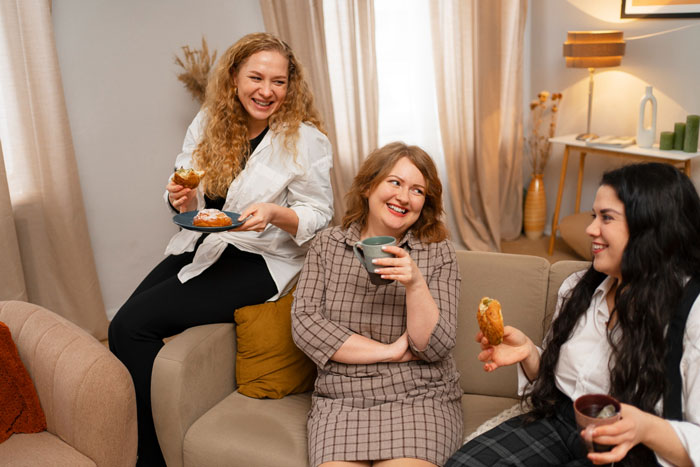 Three women happily gathered on a couch, enjoying snacks and drinks, reflecting family moments.