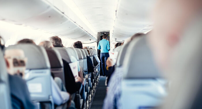 A cabin crew member walking down an airplane aisle, anticipating unhinged questions from passengers.