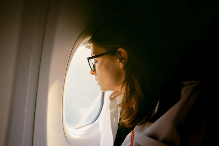 Woman looking out airplane window, reflecting on unhinged questions cabin crew have been asked.
