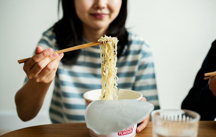 A person eating noodles from a cup, highlighting unhinged questions cabin crew have been asked.