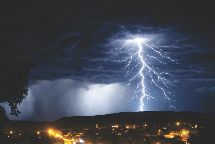 A dark, stormy sky with a bright lightning strike over a city skyline at night, relating to unhinged questions.