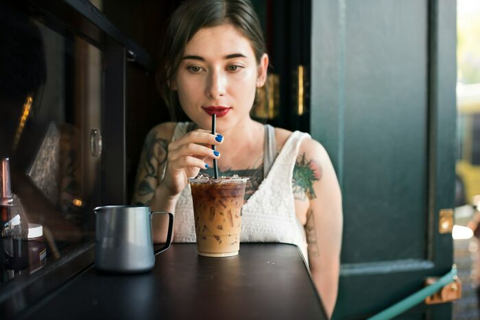 Woman with tattoos sipping an iced coffee through a straw, a common passenger activity.