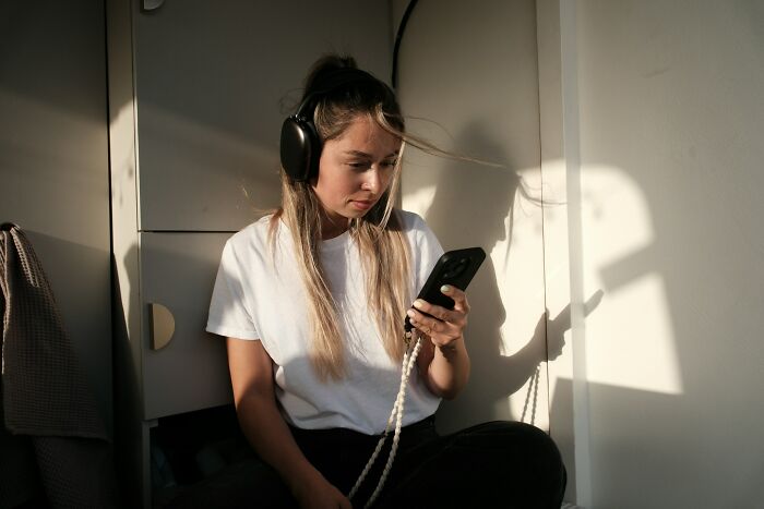 Woman wearing headphones, looking at her phone, representing passengers who might have unhinged questions.