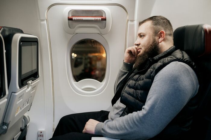 A passenger on an airplane looking out the window, possibly pondering unhinged questions for cabin crew.
