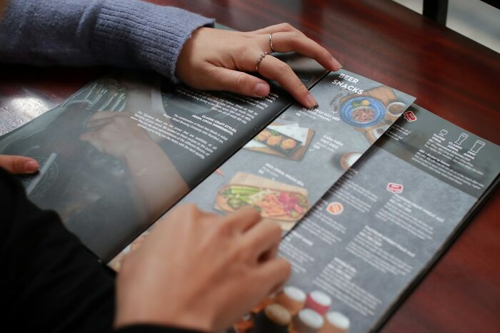 Hands holding a menu open to the beer and snacks section, illustrating common unhinged questions asked to cabin crew.