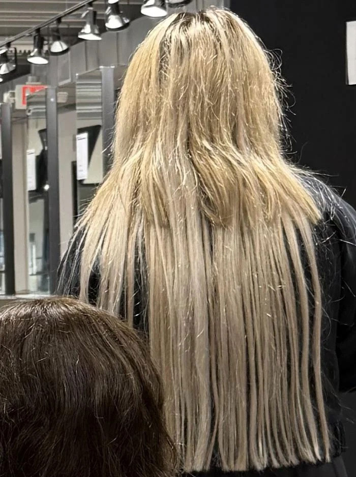 A woman with long, blonde, uneven hairstyles, with some strands significantly shorter than others, suggesting a bold and unconventional cut.